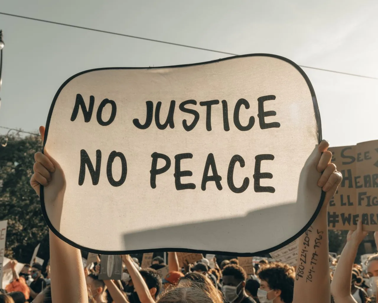 Protestors’ hands holding a sign that says "NO JUSTICE NO PEACE"
